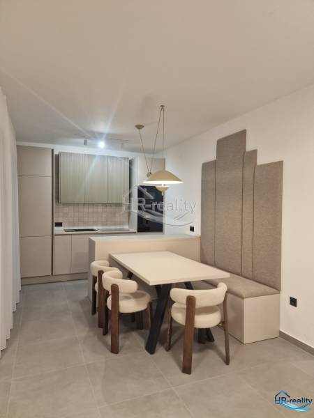 Rogoznica, Zečevo - Jedáleň v rekreačnom apartmáne s kuchyňou, svetlými stoličkami a šedými panelmi na stene.