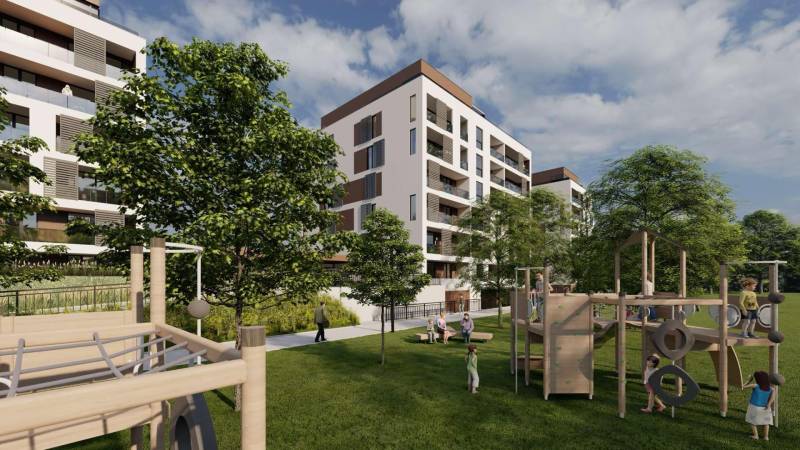 2i byt  A.3.1 - Bell Residence - Na ulici Suchoňova sú bytové domy obklopené zelenými stromami, pred ktorými sa nachádza ihrisko a ľudia.