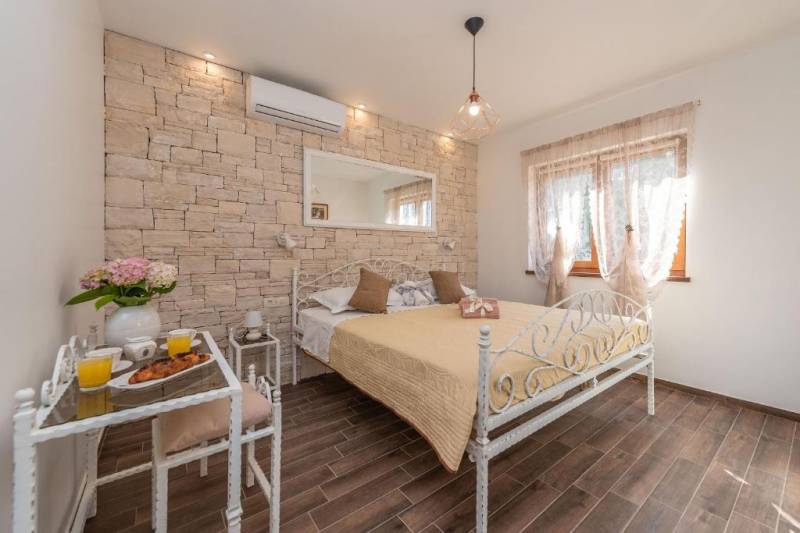 CHORVÁTSKO - Moderný rodinný dom - BIBINJE, ZADAR - Spálňa s kamennou stenou, kovovou posteľou a stolíkom s nápojmi v rodinnom dome.