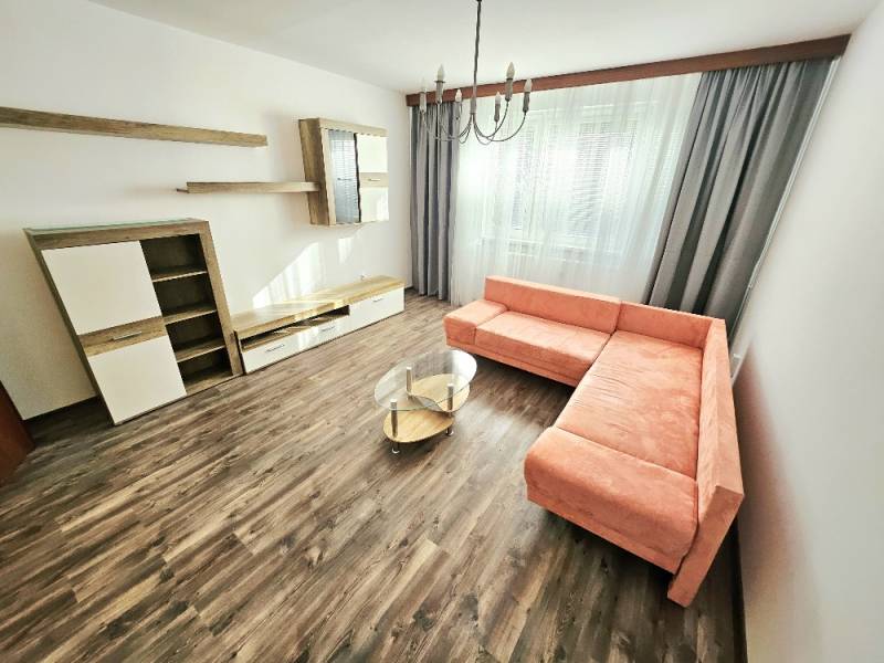 PRENÁJOM 3 IZBOVÝ BYT / 70 M2 /VEĽKOMETRÁŽNY/DUBNIČKA /LOGGIA - Obývačka 3-izbového bytu s rohovou sedačkou, závesmi a drevenou podlahou.