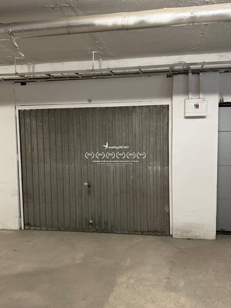 REZERVOVANÉ podzemná garáž Bratislava Nové Mesto - Kovová brána v garáži s potrubím a elektrickým rozvádzačom na stene.
