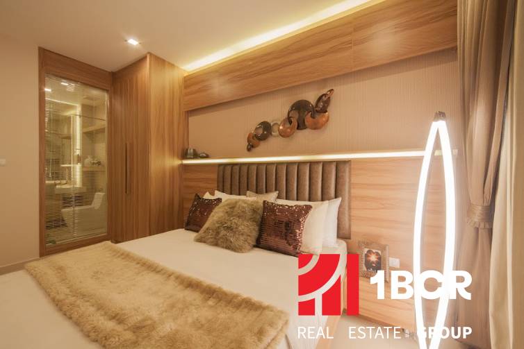 2 IZBOVÝ APARTMÁN (2 SPÁLNE + 1 OBÝV. IZBA) CITY GARDEN TOWER PATTAYA - Spálňa v 3-izbovom byte so zrkadlom, drevenými prvkami a jemným osvetlením.