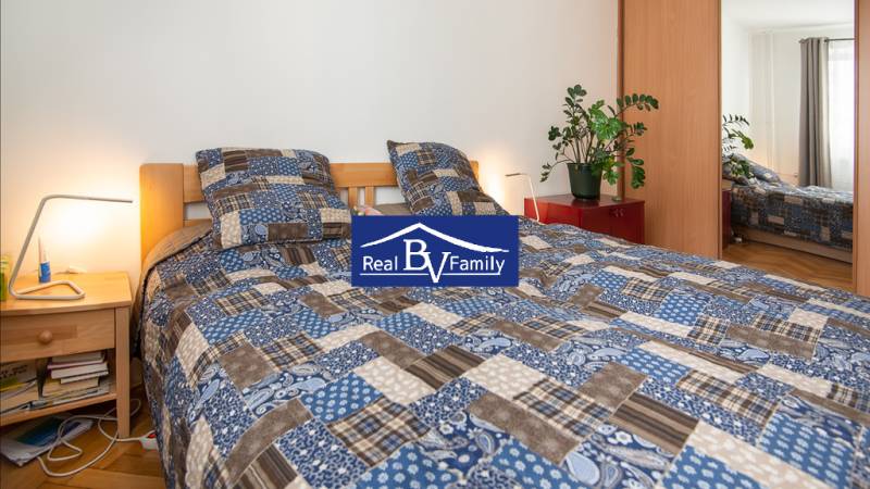 PRENÁJOM, STROMOVÁ, NOVÉ MESTO - DVOJGARSÓNKA - Spálňa v dvojgarsónke s modrobielou posteľnou bielizňou, rastlinami a nočným stolíkom.