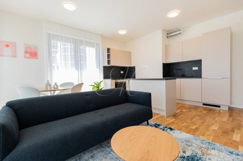 Skvelý slnečný 3i byt s balkónom v projekte METROPOLIS - Obývačka a kuchyňa v 3-izbovom byte s pohovkou, stolíkom a jedálenským stolom.