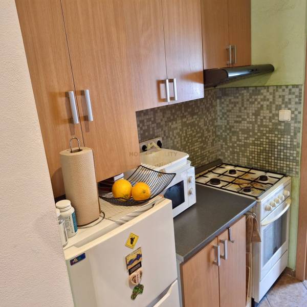 Predaj 1 izbový byt, Karpatská ulica, Bratislava I. Staré Mesto - Kuchyňa v 1-izbovom byte s plynovým sporákom, mikrovlnkou a bielou chladničkou.