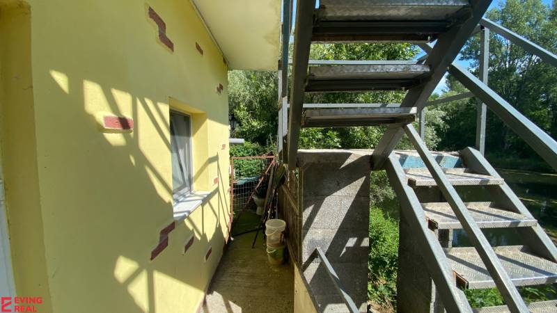 Penzión s 13 izbami na predaj, Dunajská ul., Tomášov - Úzka ulička pri žltej budove s vonkajším schodiskom, okolité stromy vrhajú tieň.