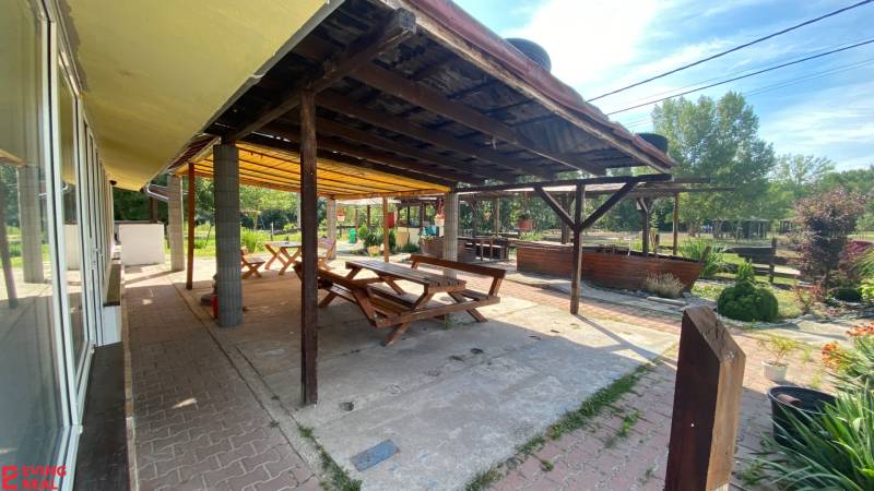 Penzión s 13 izbami na predaj, Dunajská ul., Tomášov - Na ulici Dunajská je terasa so stolmi a lavicami pri hoteloch, obklopená prírodou.