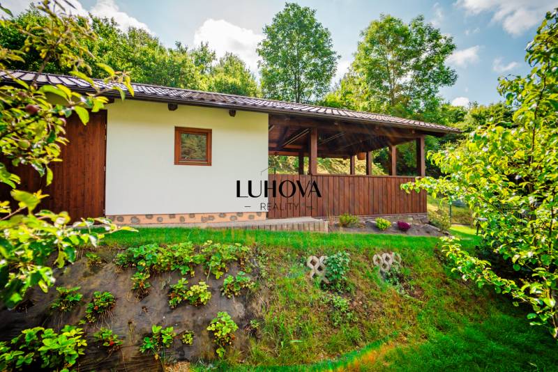 Pozemok na stavbu domu alebo ako rekreačný_Pružina - Chata na pozemku na bývanie v Pružine, obklopená zeleňou a stromami.