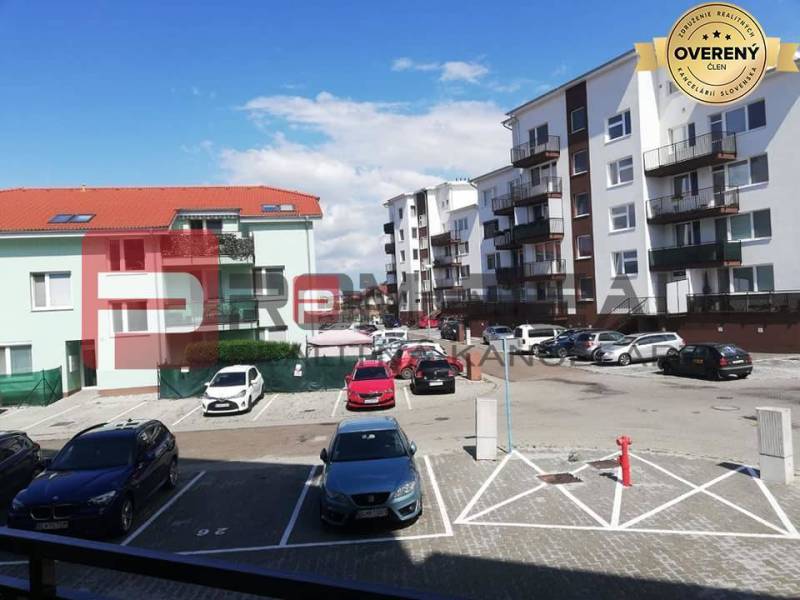 Na PRENÁJOM 2 izbový byt s garážovým státím v novostavbe - Parkovisko na ulici Slavomírova s autami pred budovami v mestskom prostredí.