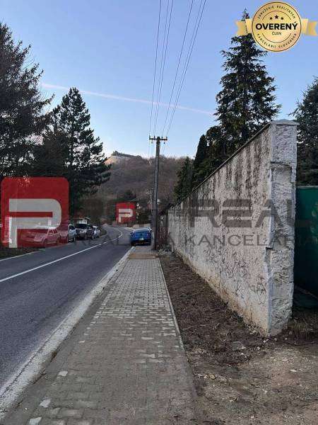Novostavba rodinného domu v Malých Karpatoch - Cesta s chodníkom vedúcim cez Pezinok pri rodinnom dome, v pozadí kopcovitá krajina.