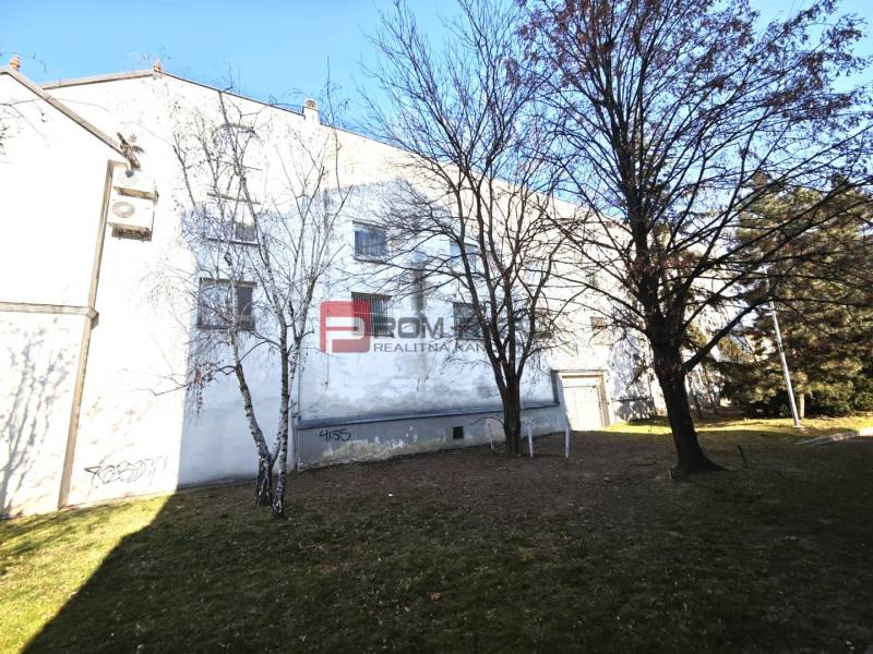 EXKLUZÍVNA INVESTÍCIA: MULTIFUNKČNÁ BUDOVA NA PREDAJ, TRNAVA - Budova so zeleňou a stromami na ulici Ľ. Podjavorinskej, v pozadí modrá obloha.