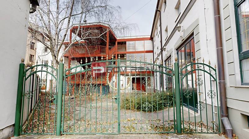 EXKLUZÍVNA INVESTÍCIA: MULTIFUNKČNÁ BUDOVA NA PREDAJ, TRNAVA - Záhrada pred budovou na Ľ. Podjavorinskej ulici v Trnave, so zeleným kovovým plotom.