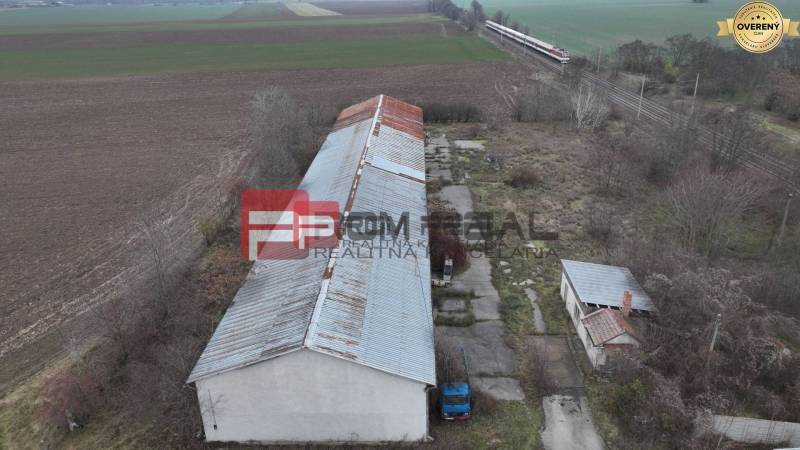 PRENÁJOM Veľký sklad s veľkorysým pozemkom v intraviláne - Na obrázku sú sklady a haly na ulici Partizánska, obklopené poľami a železnicou.