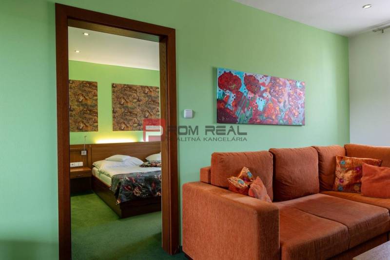 PREDAJ B&B Hotel v Starom meste - škola, centrum medicíny - Interiér penziónu s oranžovou sedačkou, obrazmi a posteľou s pestrými prikrývkami.