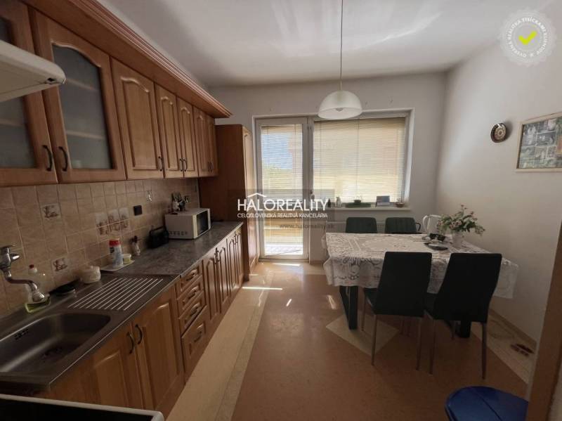 Predaj, trojizbový byt Selice - Kuchyňa v 3-izbovom byte s jedálenským stolom, skrinkami a balkónovými dverami.