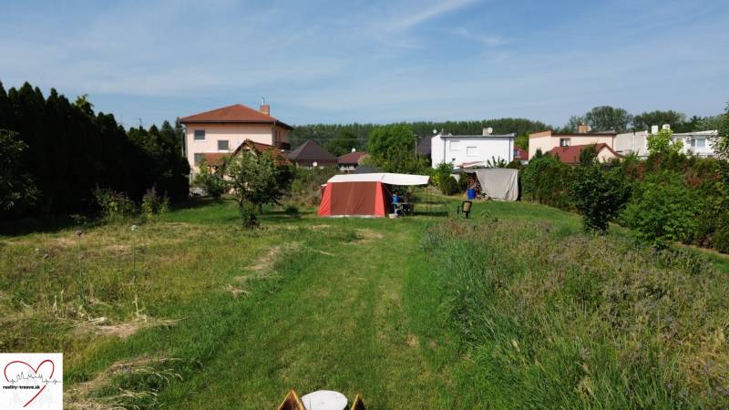 Stavebný pozemok s veľkou záhradou a potenciálom - Záhrada s trávnikom v Dolnom Bare, s výhľadom na domy a stan. Pozemky - bývanie.