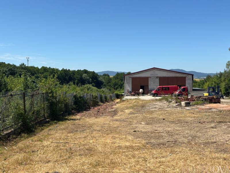 Na prenájom hala s pozemkom 4500 m² – Mníchova Lehota  - Hala so zaparkovaným autom v Mníchovej Lehote, obklopená zeleňou a oplotením.
