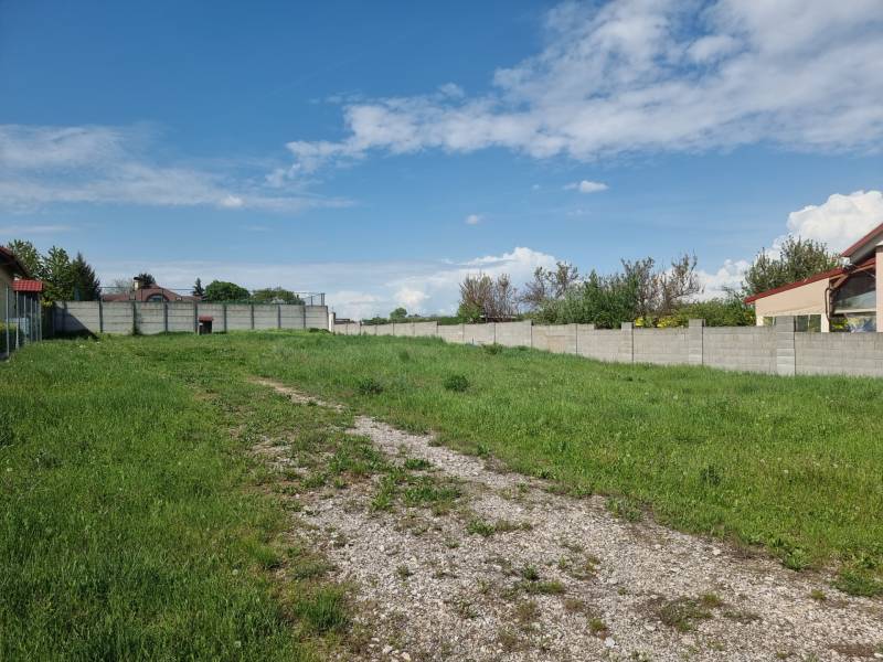 PREDAJ - Krásny rovinatý pozemok 1090 m2 - Cabaj-Čápor - Pozemok na bývanie v Cabaji-Čápore obklopený trávnatým prostredím a plotmi pod modrým nebom.