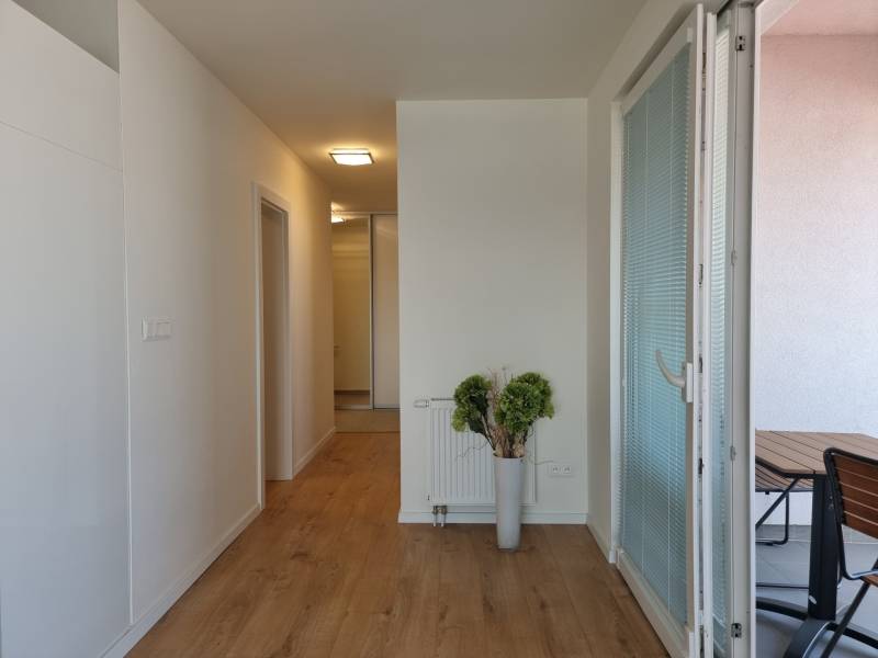 PRENÁJOM - Nový priestranný byt - Nitra, Centrum - Chodba so svetlým dreveným podlahovým povrchom v 2-izbovom byte, priestor otvorený na balkón.