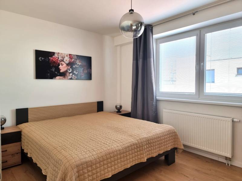 PRENÁJOM - Nový priestranný byt - Nitra, Centrum - Spálňa v 2-izbovom byte s posteľou, obrazom na stene a veľkým oknom.