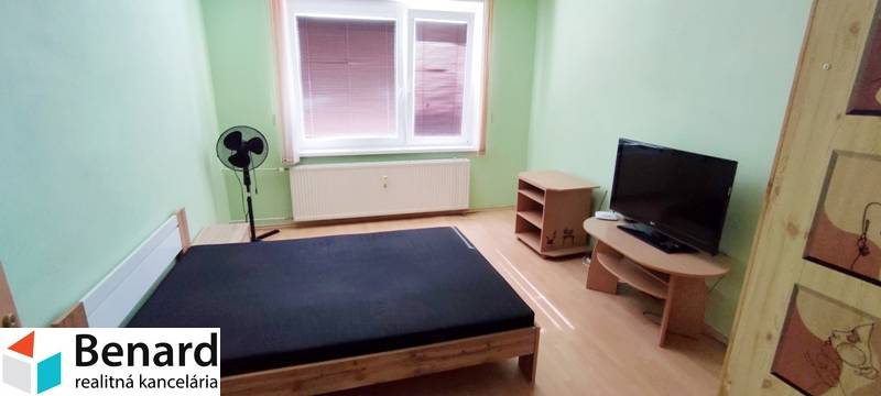 2 IZBOVÝ BYT NA PREDAJ, 59 m2, PREŠOV- PROSTĚJOVSKÁ UL. - Spálňa v 2-izbovom byte s posteľou, televízorom a ventilátorom v rohu miestnosti.