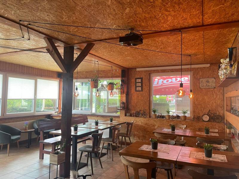 Pozemok s gastronomickým zariadením, kompletné zariadenie a zázemie - Interiér gastro priestorov so stolmi, dreveným obkladom a dekoratívnymi svetlami.