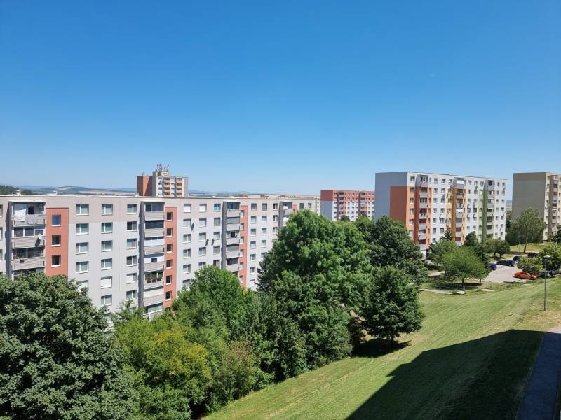 PREDAJ- Priestranný 2 izbový byt s krásnym výhľadom - Nitra, Klokočina - Sídlisko s panelákmi na Petzwalovej ulici v Nitre, obklopené zeleňou a modrou oblohou.