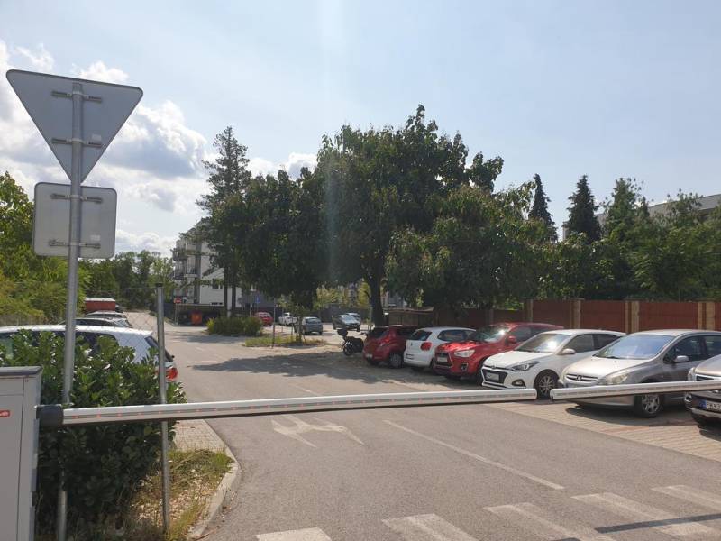 Nový priestranný 3iz. byt s klimatizáciou, balkónom a parkovaním. - Parkovisko na ulici Za dráhou, blízko Garáže, bariéra a stromy na pozadí.