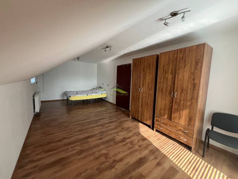 Elegantný dom v Benkovciach: Priestor, svetlo a štýl pre vašu rodinu - Podkrovná izba v rodinnom dome s posteľou, skriňami a drevenou podlahou.