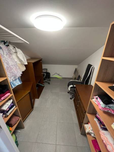 Elegantný dom v Benkovciach: Priestor, svetlo a štýl pre vašu rodinu - Šatník v rodinnom dome s policami, stoličkou a zaveseným oblečením.