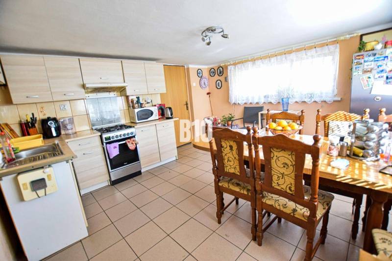 Predaj rodinného domu, Čadca - Kuchyňa v rodinnom dome s veľkým stolom, drevenými stoličkami a spotrebičmi.