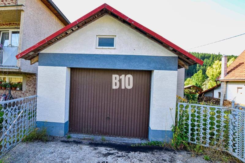 Predaj rodinného domu, Čadca - Garáž pri rodinnom dome v Turzovke, obklopená zeleňou a plotom.