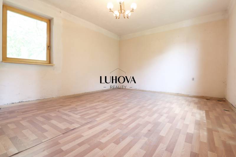 Starší rodinný dom – Ihrište_Púchov  - Prázdna miestnosť s drevenou podlahou a oknom v rodinnom dome, neutrálne steny.