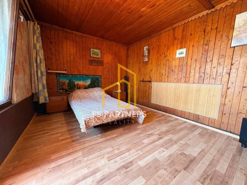 Záhrada s čiastočne prerobenou chatkou – Komárno, časť Nová Stráž - Drevený interiér so vzorovanou posteľou a obrazmi na stenách.
