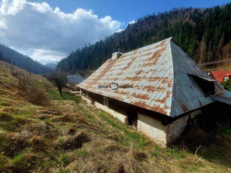 NA PREDAJ drevená chalúpka v Motyčkách  - Chata v Motyčkách obklopená prírodou, lúkami a lesom pod modrou oblohou.