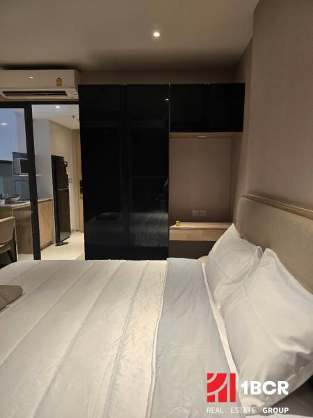 ŠTÚDIO ONCE PATTAYA - Spálňa s bielou posteľou a čiernou skriňou, vedľa kuchynskej linky.