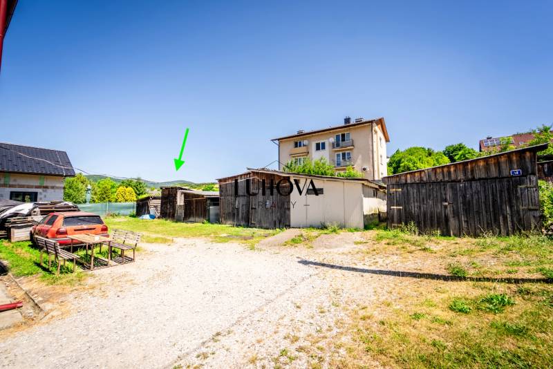 Na predaj 2-izbový byt so záhradkou a garážou! - Dvor s niekoľkými drevenými budovami a zaparkovaným autom v Púchove, pri 2-izbovom byte.