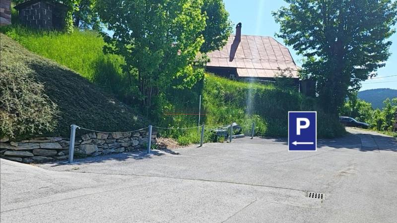 PREDAJ – Apartmánový dom na Donovaloch s 3 samostatnými apartmánmi - Parkovisko na ulici Donovaly v meste Donovaly pri rodinných domoch, so stromami a trávou.