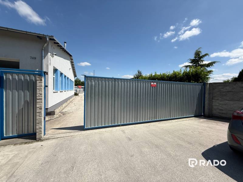 Skladová hala na prenájom 108 m², novostavba | Tureň - Brána a budova pri skladoch a halách v Tureň, modrá obloha a zeleň v pozadí.