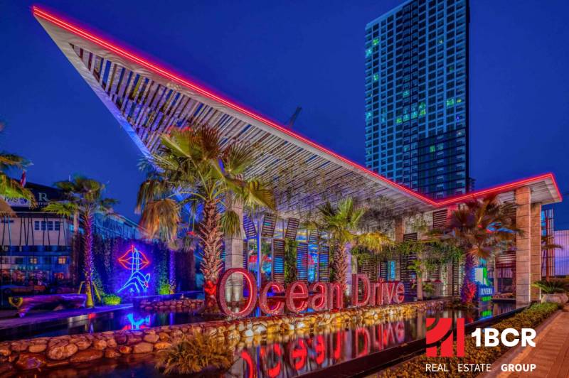 THE RIVIERA OCEAN DRIVE PATTAYA - Nočná scéna s osvetlenou budovou a nápisom v rámci výstavby bytov v Pattaye.