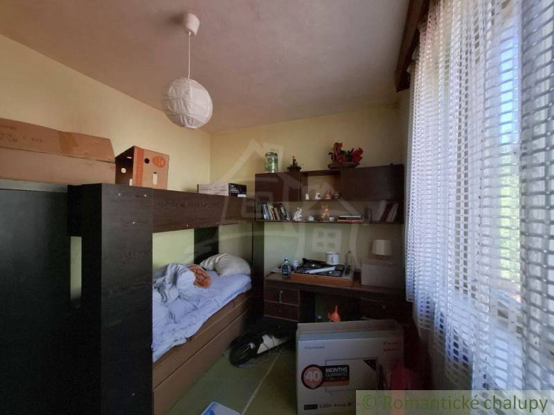 Priestranný poschodový rodinný dom v Lovinobani - Izba v rodinnom dome s posteľou, stolom a regálom.