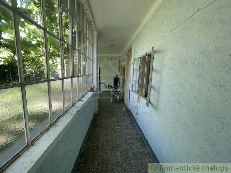 Priestranný pozemok so starším rodinným domom v obci Tvrdošovce - Zasklená veranda v rodinnom dome s výhľadom na záhradu a nábytkom.