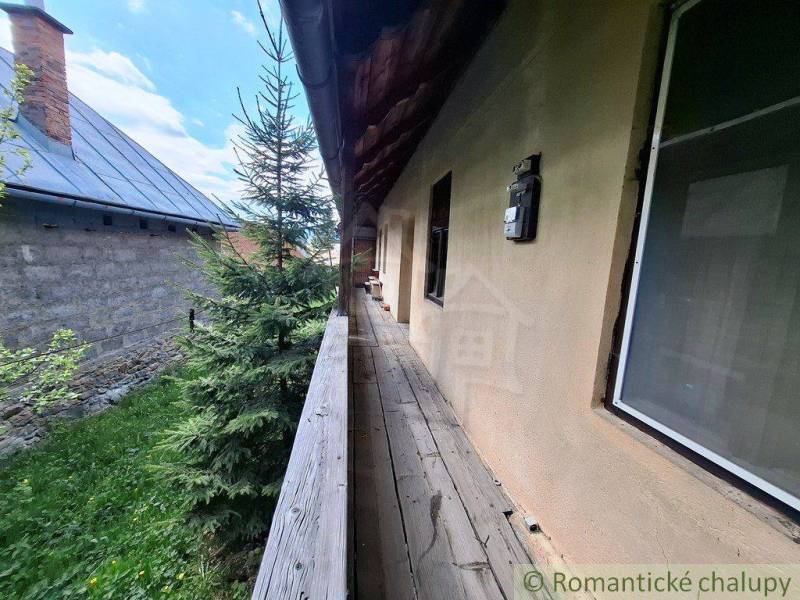 Súbor nehnuteľností určených na revitalizáciu Pohorelá -Nízke Tatry - Drevený chodník vedľa rodinného domu v Pohorelej, obklopený zeleňou a susednou budovou.