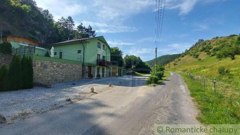 5-izbový štýlový dom pod lesom v obci Dobrá Voda na predaj - Rodinný dom v Dobrej Vode pri ceste obklopený zelenými kopcami a stromami.