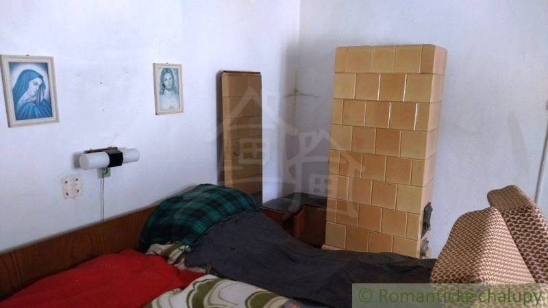 Útulný vidiecky domček, Fričovce - Izba v rodinnom dome s kachľovou pecou, posteľou a nástennými obrázkami.