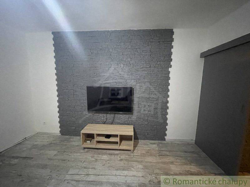 Zrekonštruovaný rodinný dom v tichej lokalite v obci Palárikovo - Televízor na kamennej stene, pod ním drevený stolík, miestnosť v rodinnom dome.