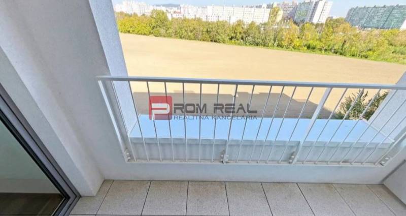 Bývajte v 2-izbovom byte priamo pri električke do centra! - Balkón 2-izbového bytu na Labutej ulici, Bratislava V s výhľadom na zeleň a budovy.