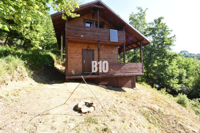 Predaj chaty a chalupy, Bytča - Drevená chata v prírode pri Bytči, obklopená stromami a ohniskom.