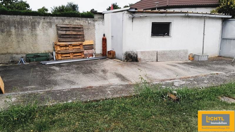 Predaj rodinného domu, Neusiedl am See - Dvor pri rodinnom dome v 2473 Potzneusiedl s betónovou plochou a drevenými paletami.