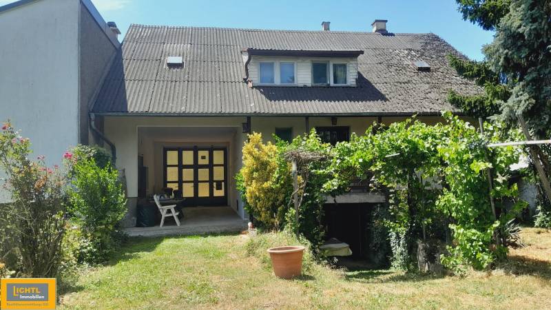 Predaj rodinného domu, Neusiedl am See - Rodinný dom v Potzneusiedli so záhradou, rastlinami a viditeľným poschodím s oknami.